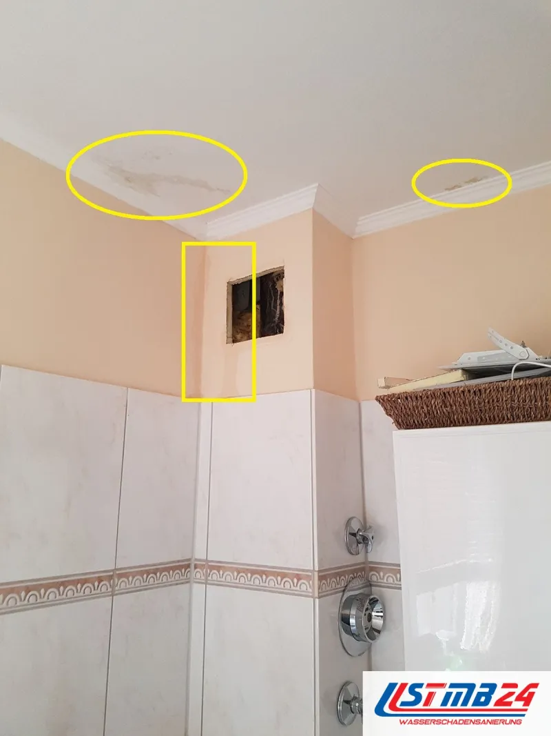 Bad mit Fliesenbordüre, Wasserflecken an der Decke gelb umkreist, darunter eine kleine Öffnung in der Wand über den Fliesen