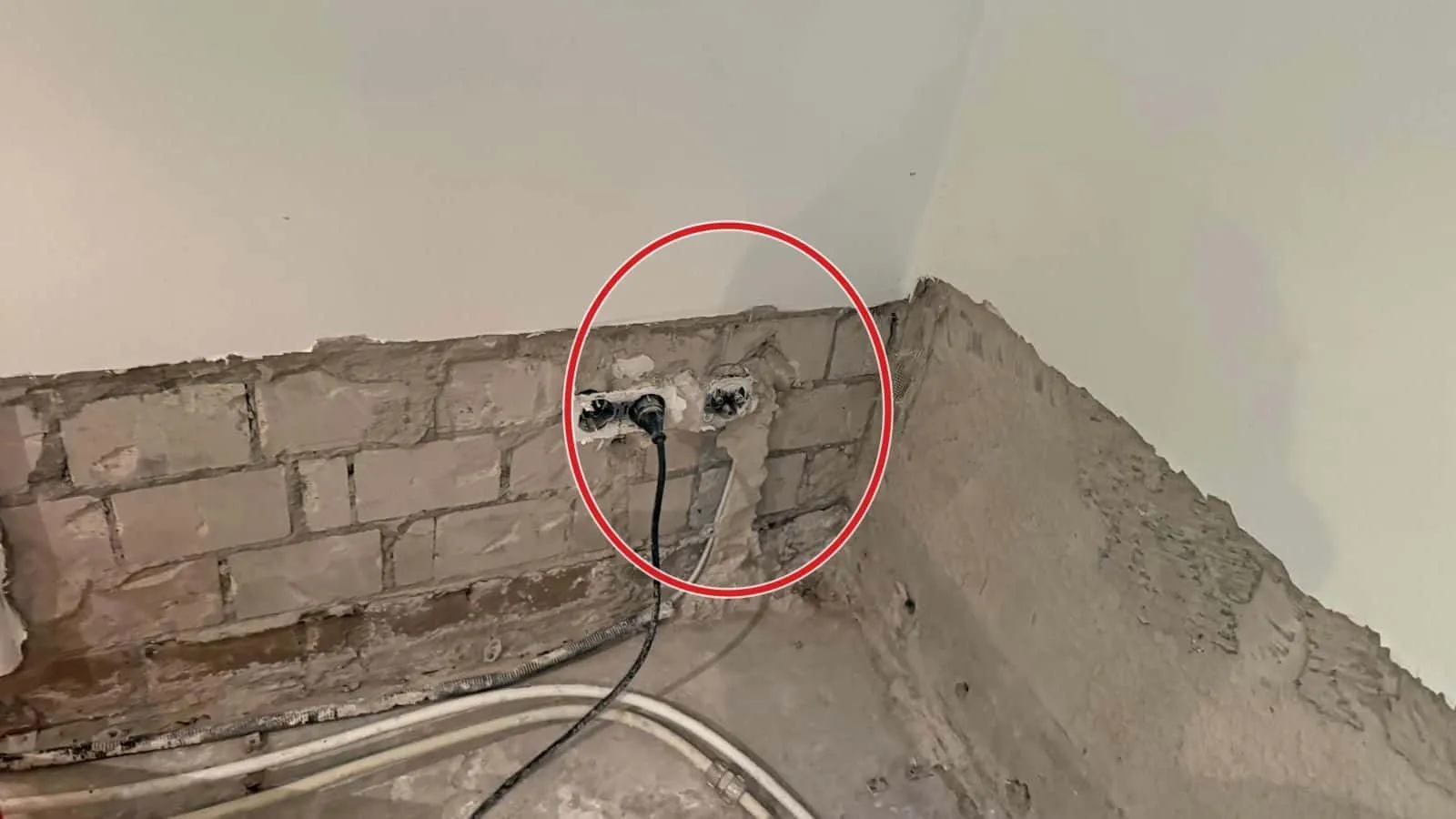 Doppelsteckdose in einer bis Kniehöhe freigelegten Kalksandsteinwand, Kabel und Schläuche am Boden