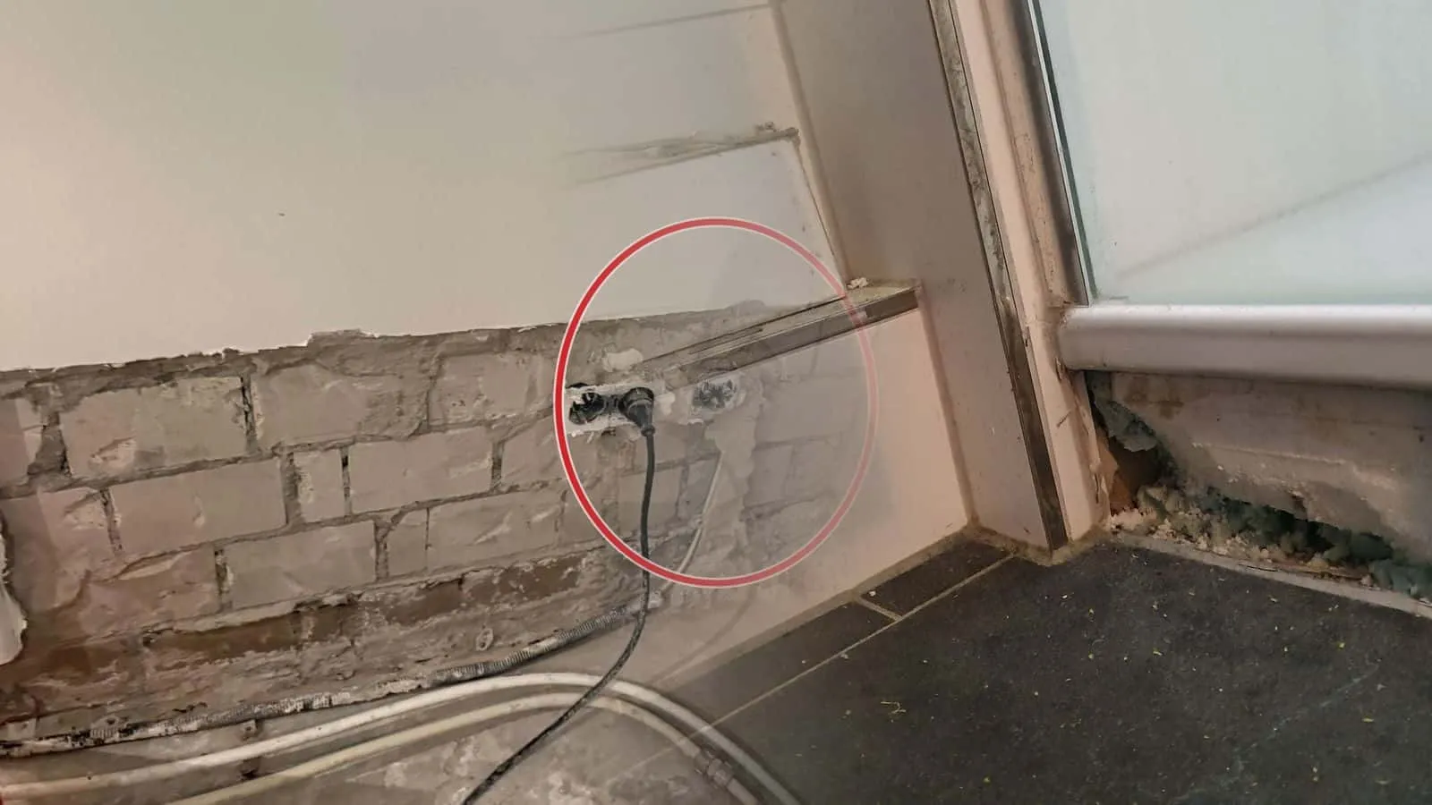Unterer Anschluss einer Balkontür mit loser Fliesenplatte auf der Fensterbank, dahinter grüne Dämmung mit Schimmelspuren