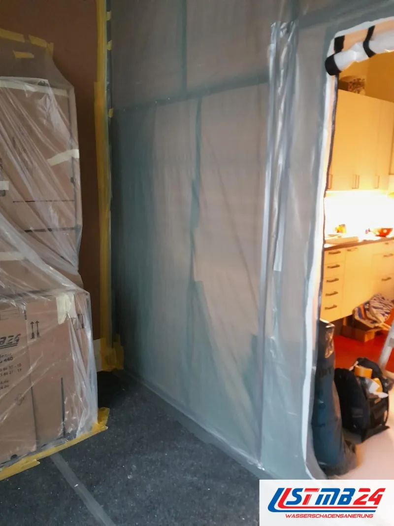Abgeklebte Folienwand mit Durchgang, davor in Folie gepackte Möbel und Kartons auf Malervlies