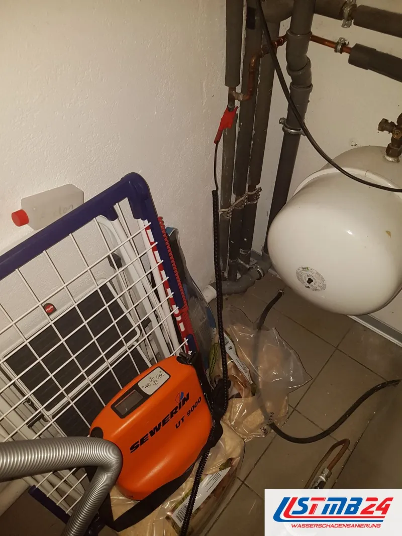 Orangefarbenes Ortungsgerät mit Schlauch im Heizungsraum, dahinter Ausdehnungsgefäß und Rohrleitungen an der Wand