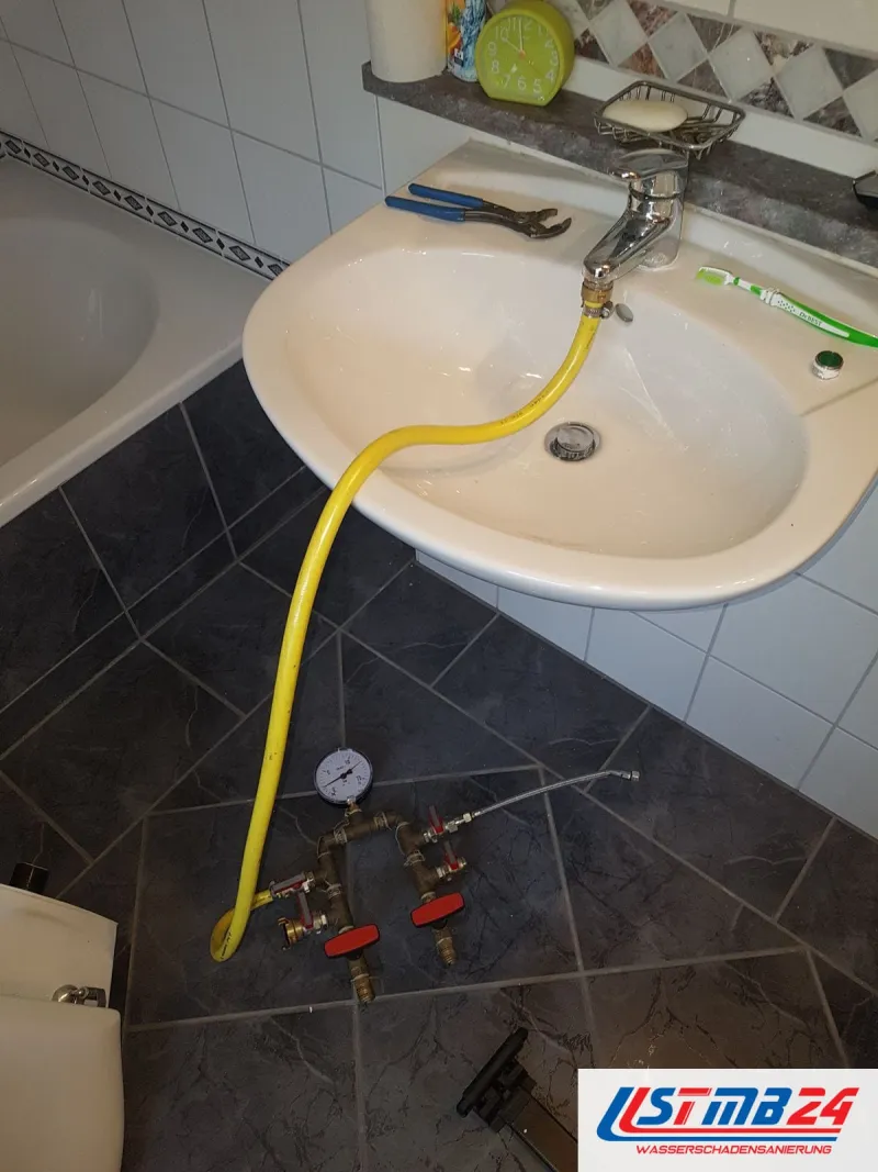 Waschbecken mit gelbem Schlauch, der zu Prüfventilen auf dunklen Bodenfliesen führt