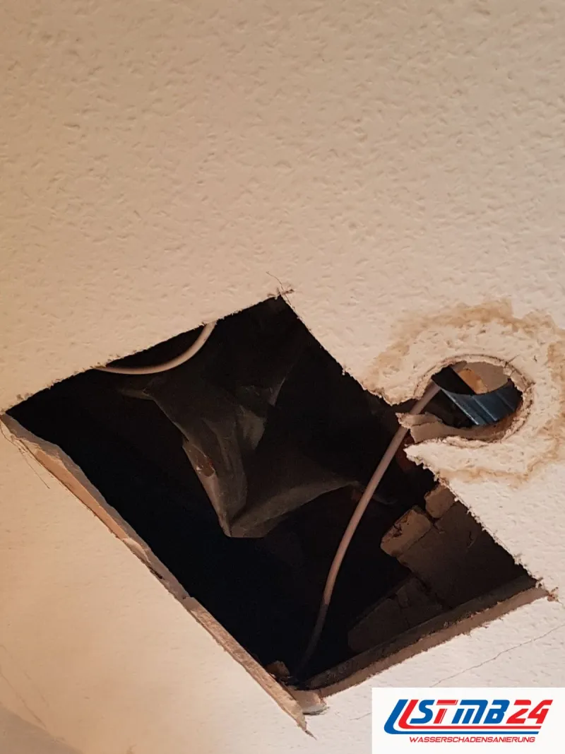 Quadratische Deckenöffnung neben einem Auslass, um den sich ein brauner Wasserrand zieht, ein Kabel hängt heraus
