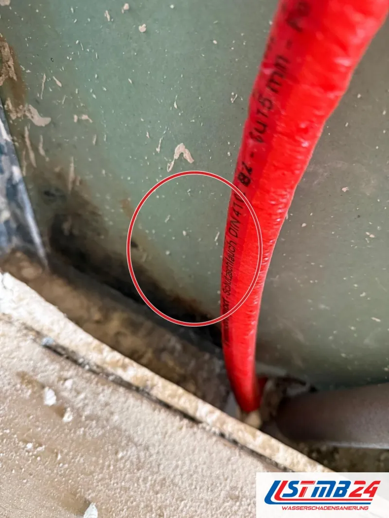 rotes Rohr im geöffneten Boden vor grüner Wandplatte, ein roter Kreis markiert die Stelle