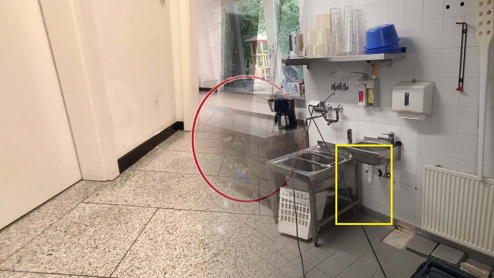 Küche eines Gastbetriebs mit Edelstahlspülen, das Handwaschbecken samt Siphon darunter gelb umrandet