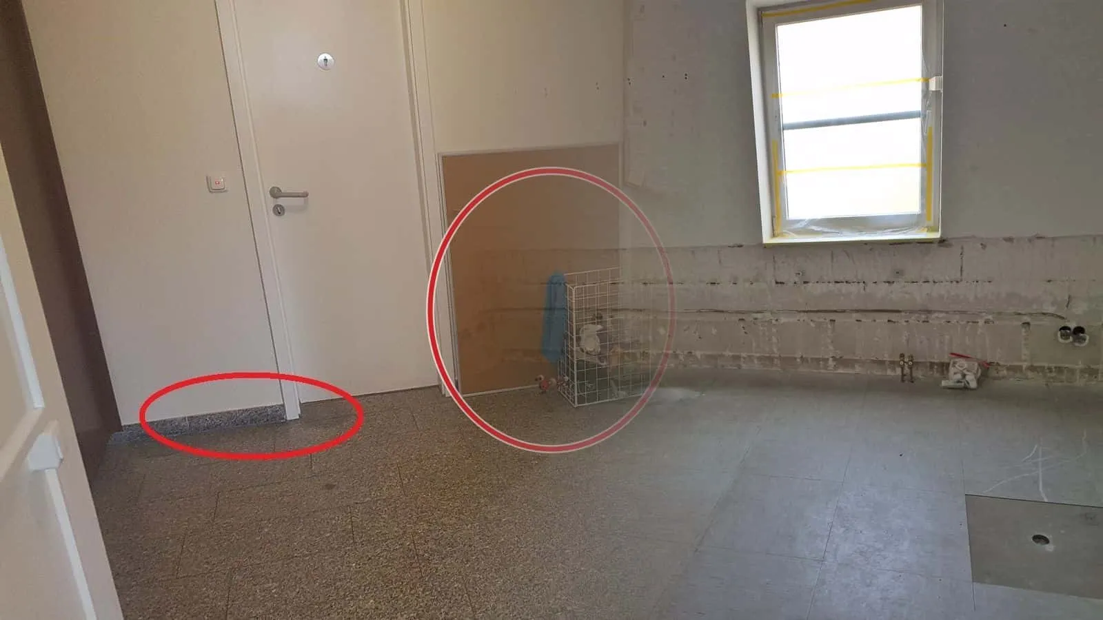 Raum mit bis auf Kniehöhe abgeschlagenem Putz, freigelegten Leitungen und zwei abgedeckten Öffnungen im Boden