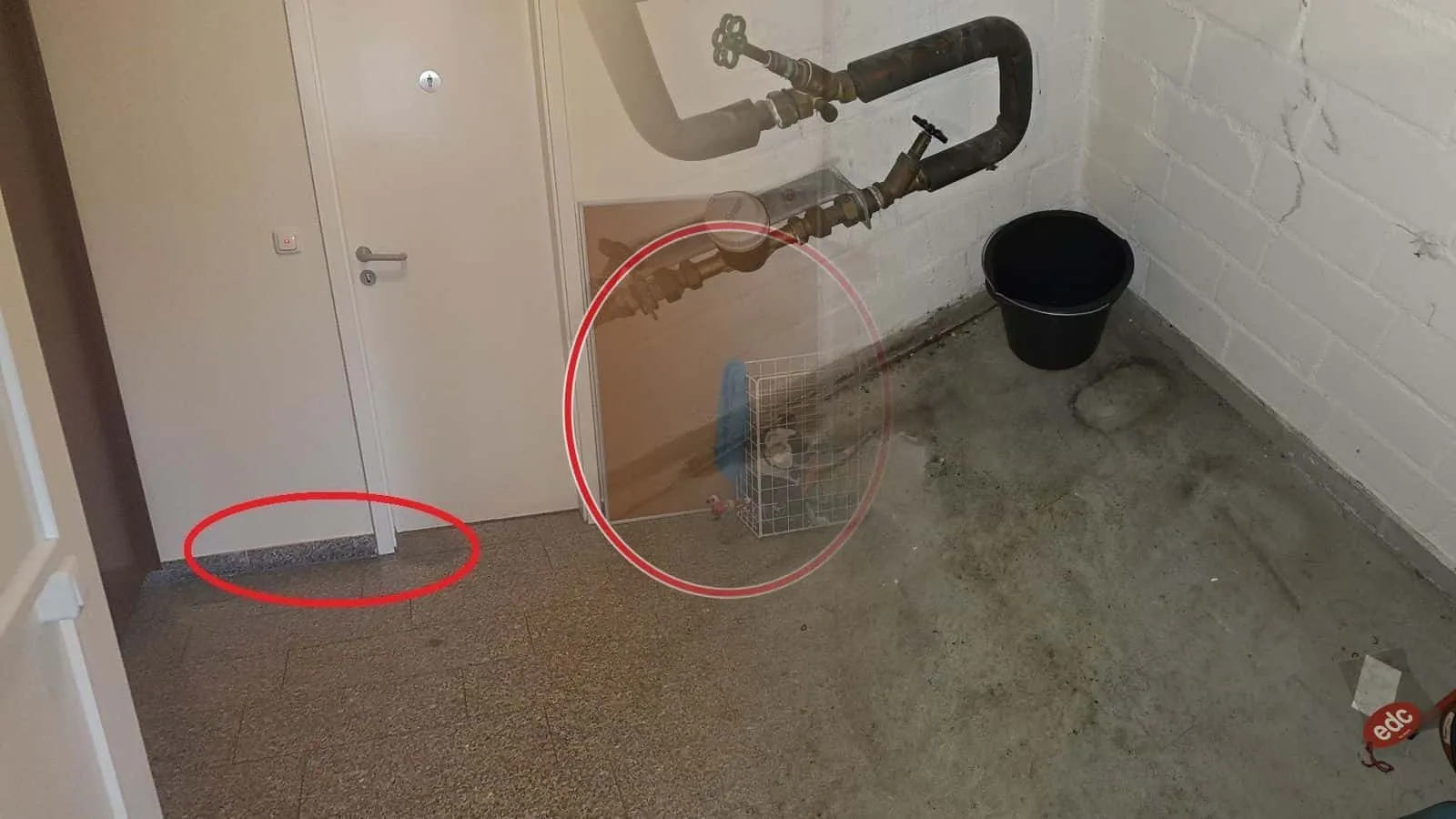 Hausanschluss im Keller mit Wasserzähler und Schrägsitzventilen, darunter ein Eimer und ein nasser Fleck