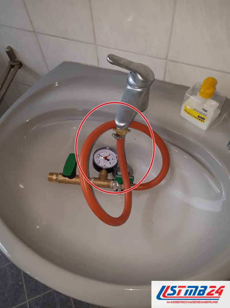 Waschbecken mit orangem Schlauch und Prüfgerät, ein roter Kreis markiert die Stelle