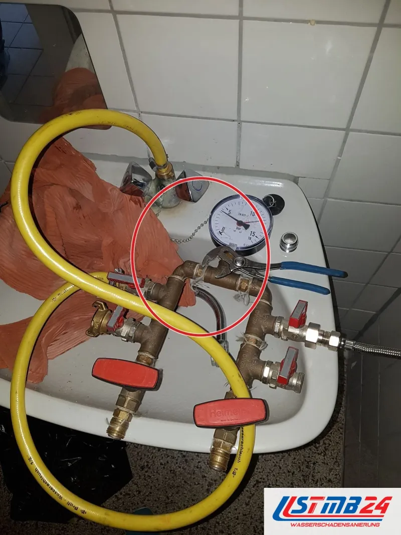 Messingverteiler mit Manometer und roten Kugelhähnen auf dem Waschbecken, gelber Schlauch, Rohrzange, ein roter Kreis markiert die Stelle