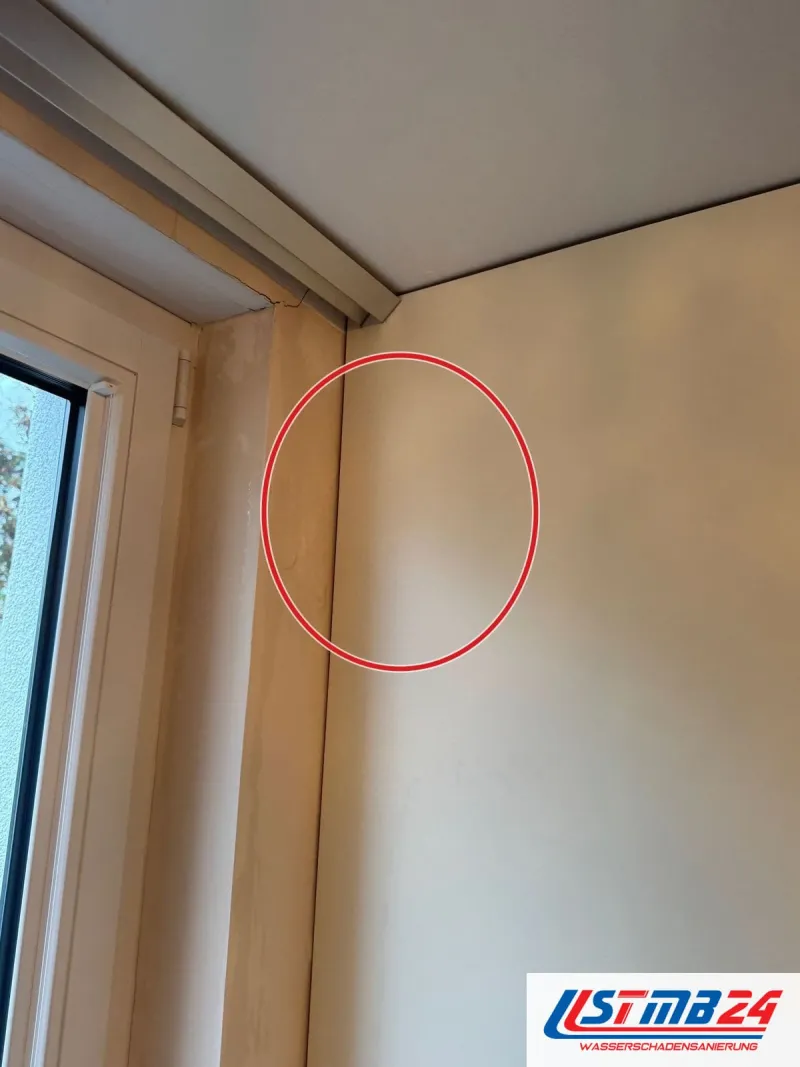 Hölzerner Fensterrahmen an einer Zimmerecke, oben eine Vorhangschiene, der Anschluss zwischen Rahmen, ein roter Kreis markiert die Stelle