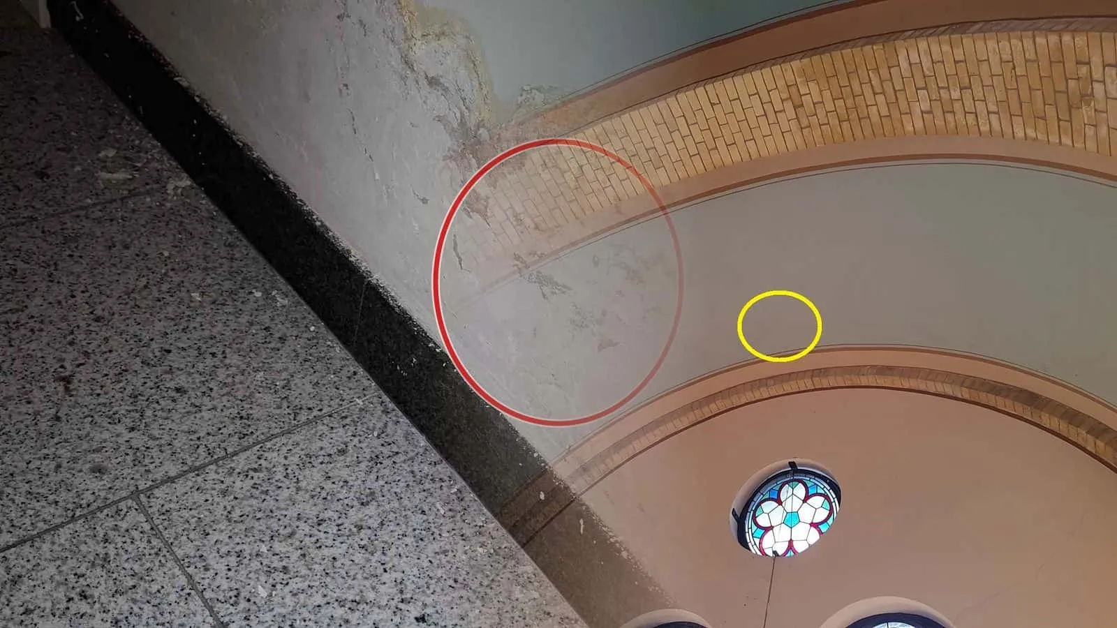 Gemauerte Bögen unter einer gewölbten Decke mit Rundfenster, ein gelber Kreis markiert den feuchten Fleck im Putz