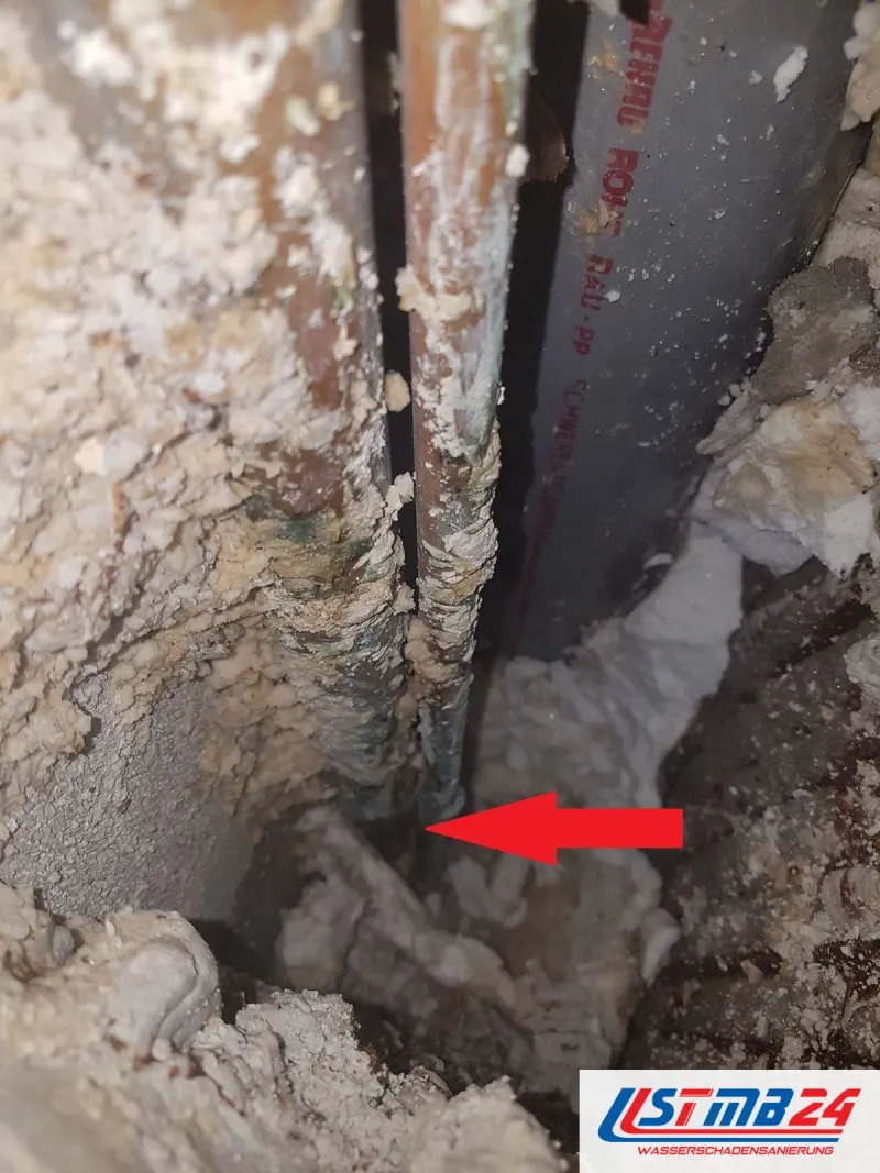 Aufgestemmte Wand mit freigelegtem Rohr, ein roter Pfeil zeigt auf die Bruchstelle im Mauerwerk