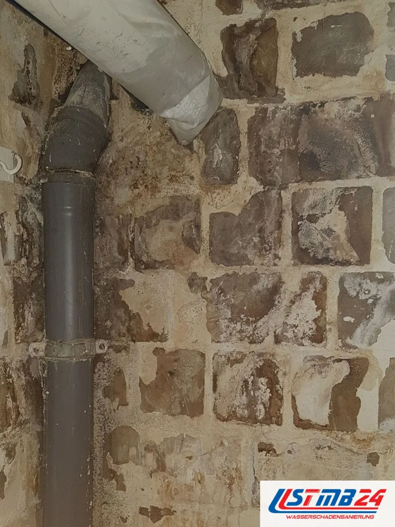 Wand mit abgeschlagenem Putz und Mauerwerk neben einem grauen Fallrohr