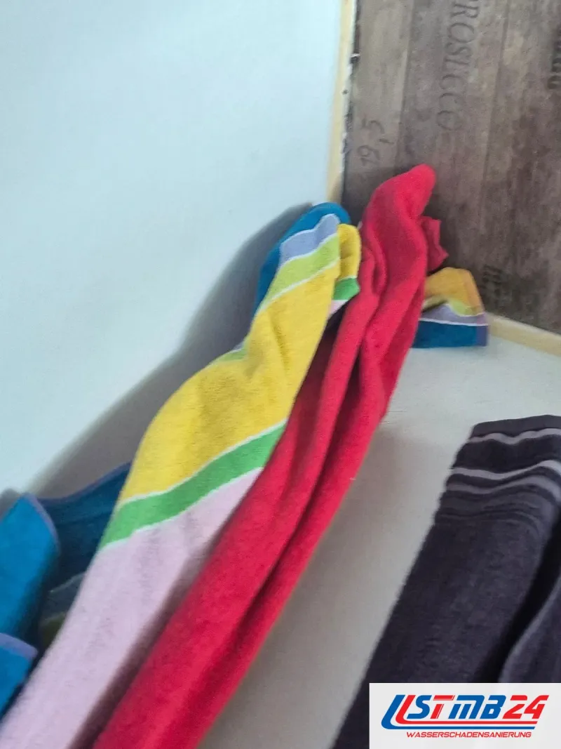 Bunte Handtücher liegen vor der Badewanne und saugen Wasser auf