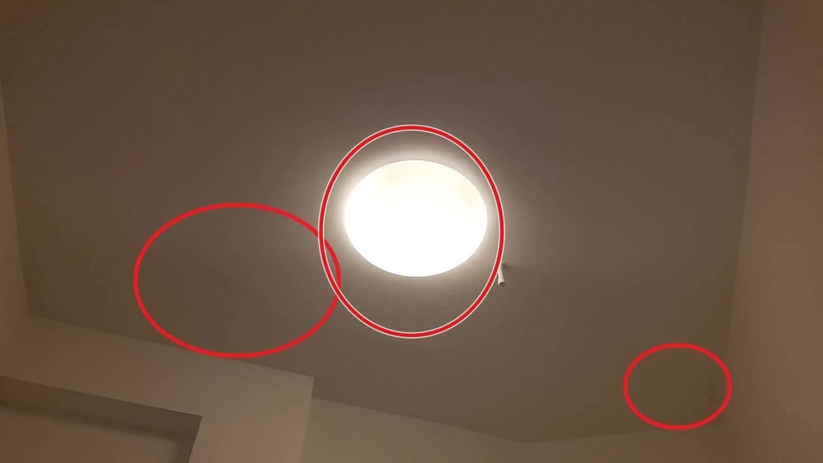 Zimmerdecke mit runder Deckenleuchte, zwei rote Kreise markieren feuchte Stellen neben der Lampe und in der Ecke