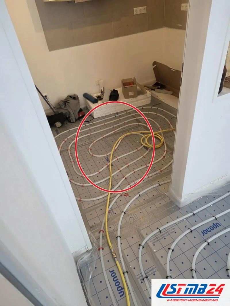 Neu verlegte Fußbodenheizung mit Rohrschlangen auf Noppenplatten in zwei Räumen, ein roter Kreis markiert die Stelle