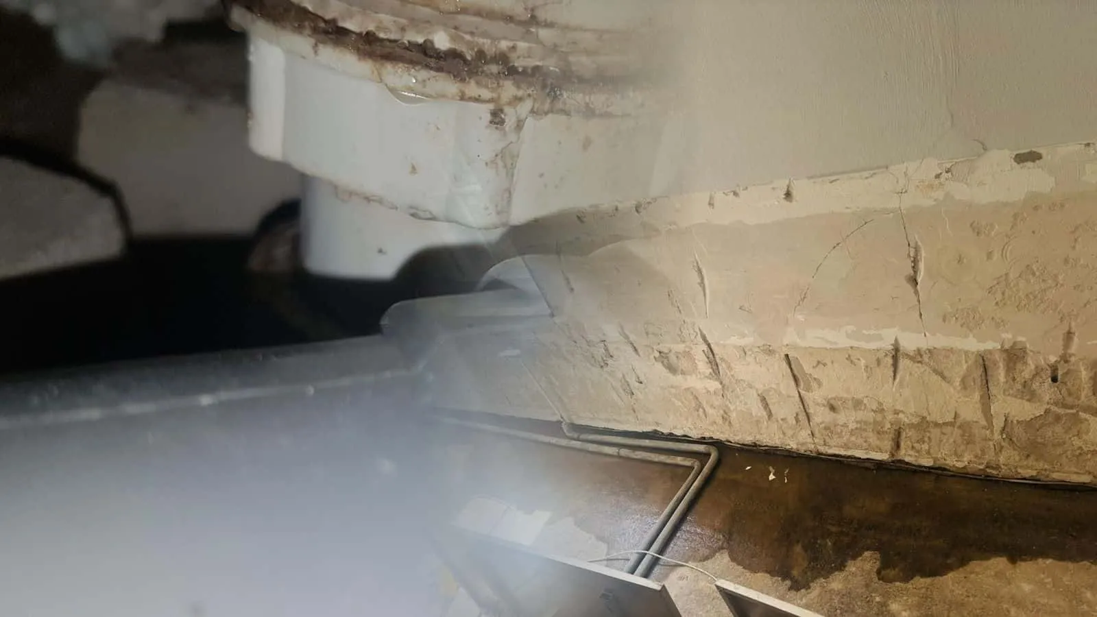Wand mit bis zur halben Höhe abgeschlagenem Putz unter einem Fenster, am Boden davor steht noch Wasser