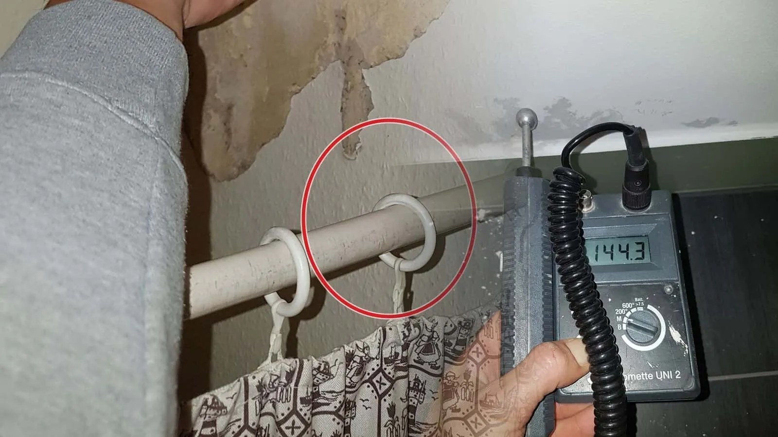 Messgerät mit Anzeige 144,3 vor Flecken an einer Wand über dunklem Boden