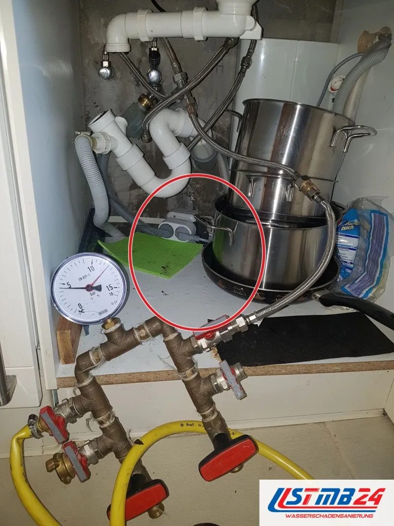 Offener Spülenschrank mit Töpfen und Siphon, davor eine Prüfarmatur, ein roter Kreis markiert die Stelle