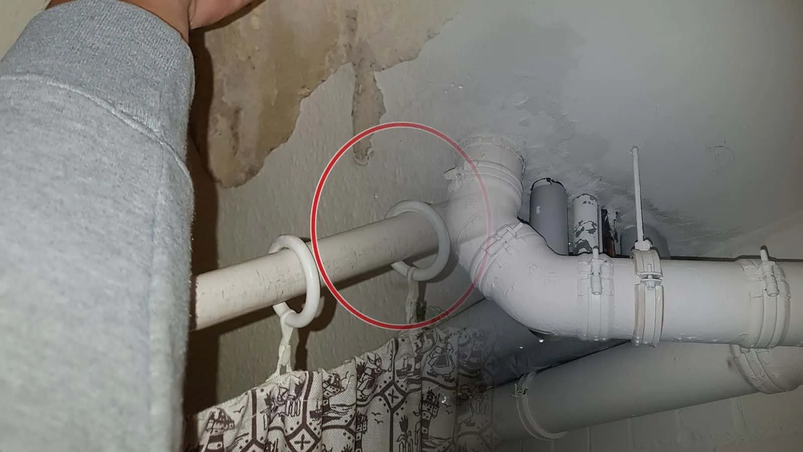 Weiße Abflussrohre mit Bogen unter einer Kellerdecke, darüber ein dunkler Fleck an der Decke