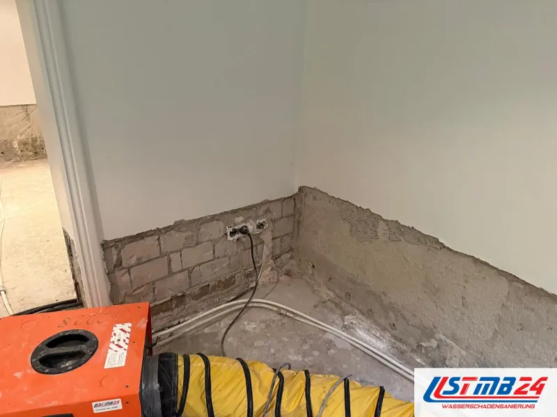 Rotes Heizgerät mit gelbem Warmluftschlauch vor einer Wand, deren Putz unten bis aufs Mauerwerk abgeschlagen ist, Dosen freigelegt