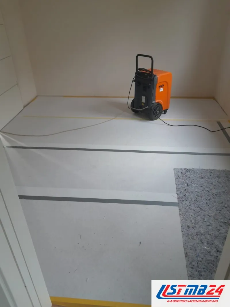Oranger Kondenstrockner auf Abdeckpappe in einem leeren Zimmer, Vlies und Klebeband schützen den Boden, Kabel am Gerät