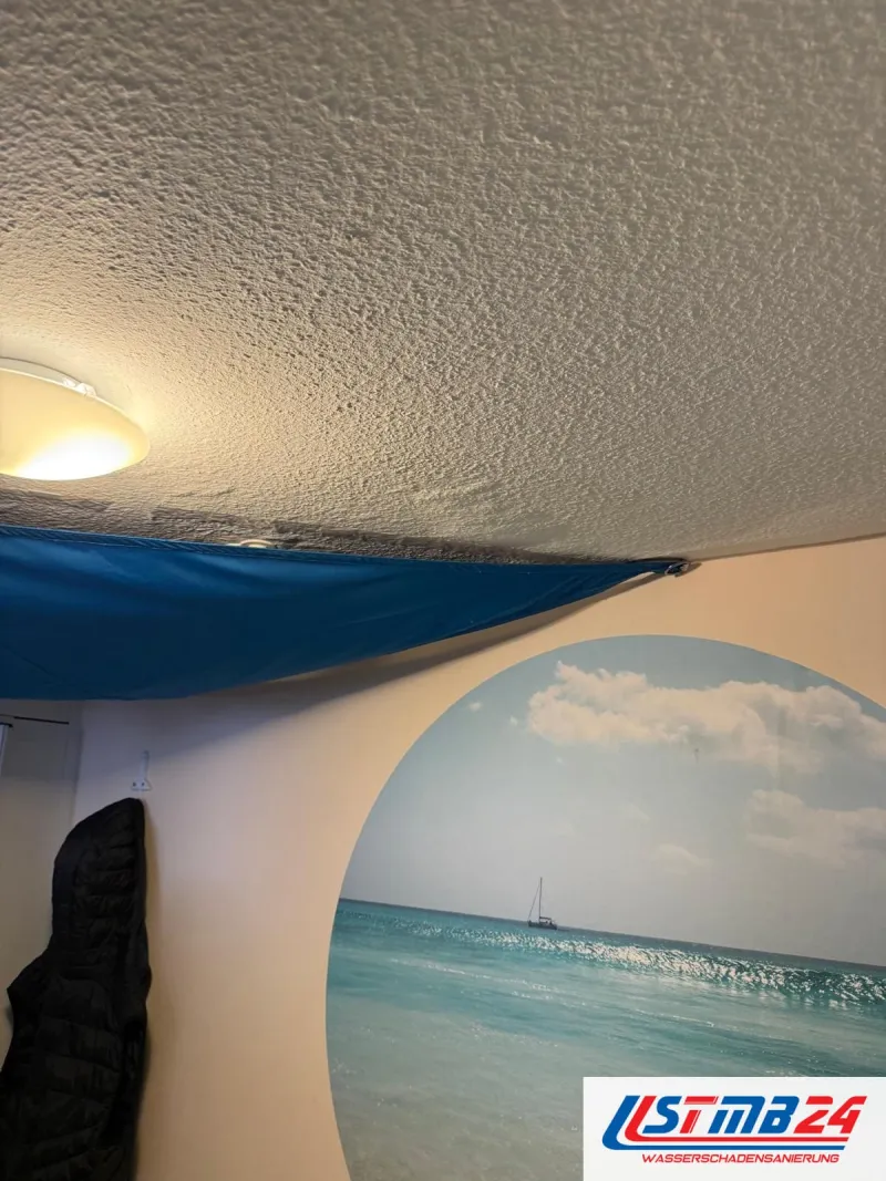 Blaue Plane unter einer durchnässten Zimmerdecke gespannt, Deckenlampe darüber, rundes Wandbild im Raum