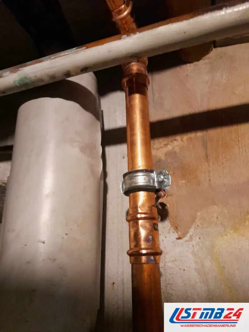 Kupfersteigleitung mit verschraubter Reparaturschelle über einem Pressfitting, gedämmte Leitung daneben, Wasserspur am Putz