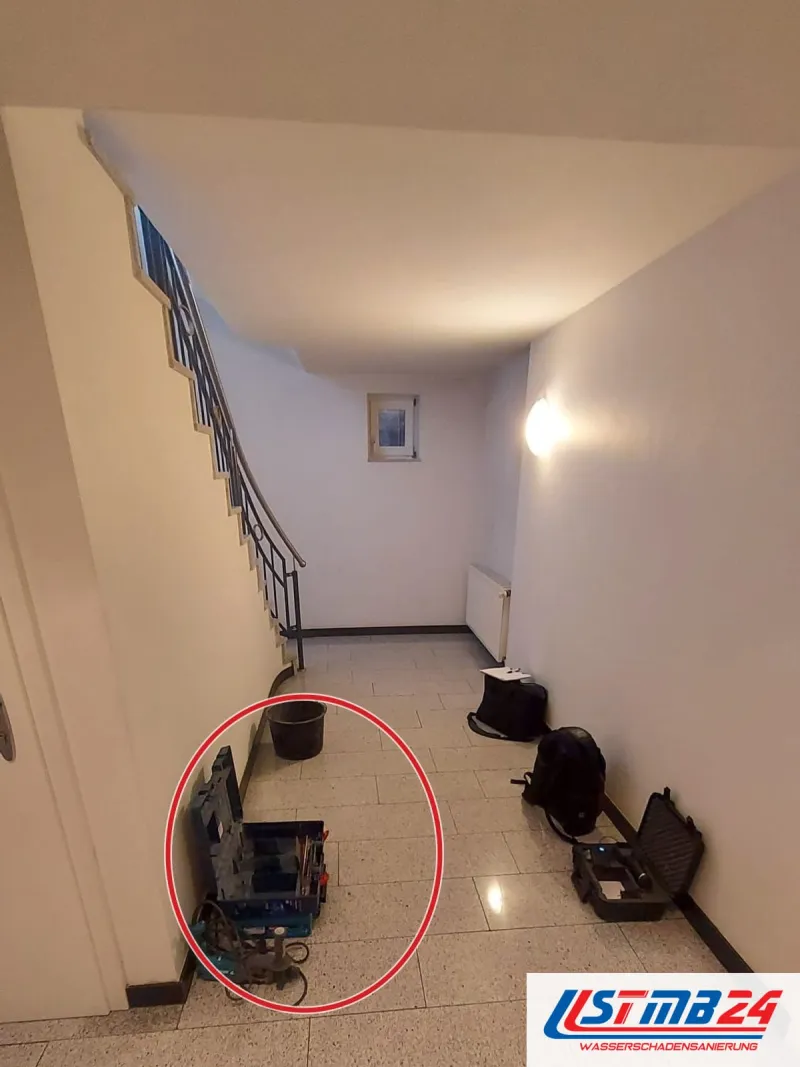 Werkzeugkoffer, Messkoffer, Rucksack und Eimer stehen im Hausflur unter der Treppe, ein roter Kreis markiert die Stelle