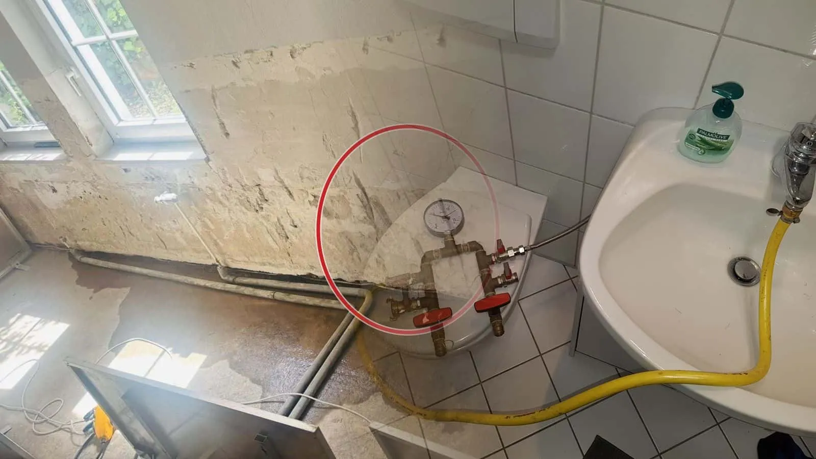 Prüfarmatur mit Manometer und zwei roten Kugelhähnen auf einem WC-Deckel, der gelbe Schlauch führt zum Zulauf
