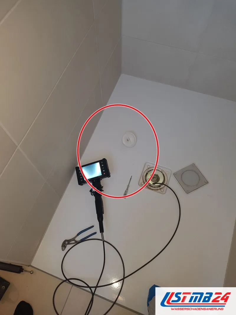 Videoendoskop mit Monitor in der Duschtasse, das Kabel steckt im offenen Bodenablauf, daneben Werkzeug, ein roter Kreis markiert die Stelle