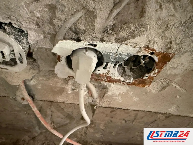 Elektroinstallation in der feuchten Wand: Doppelsteckdose mit Rostspuren, ein Stecker steckt noch, daneben eine offene Dose