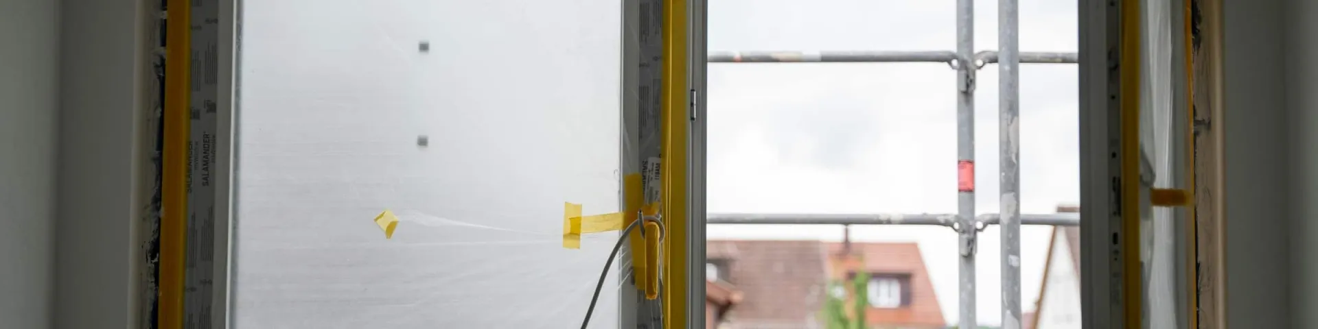 Fenster und Türen: neu eingebaute Fensterelemente mit Schutzfolie, draußen ein Baugerüst