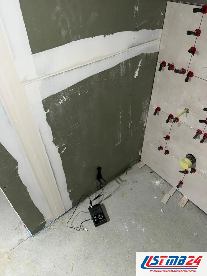 Fliesenarbeiten im Neubau: großformatige Wandfliesen mit roten Nivellierlaschen, daneben grüne Gipsplatten