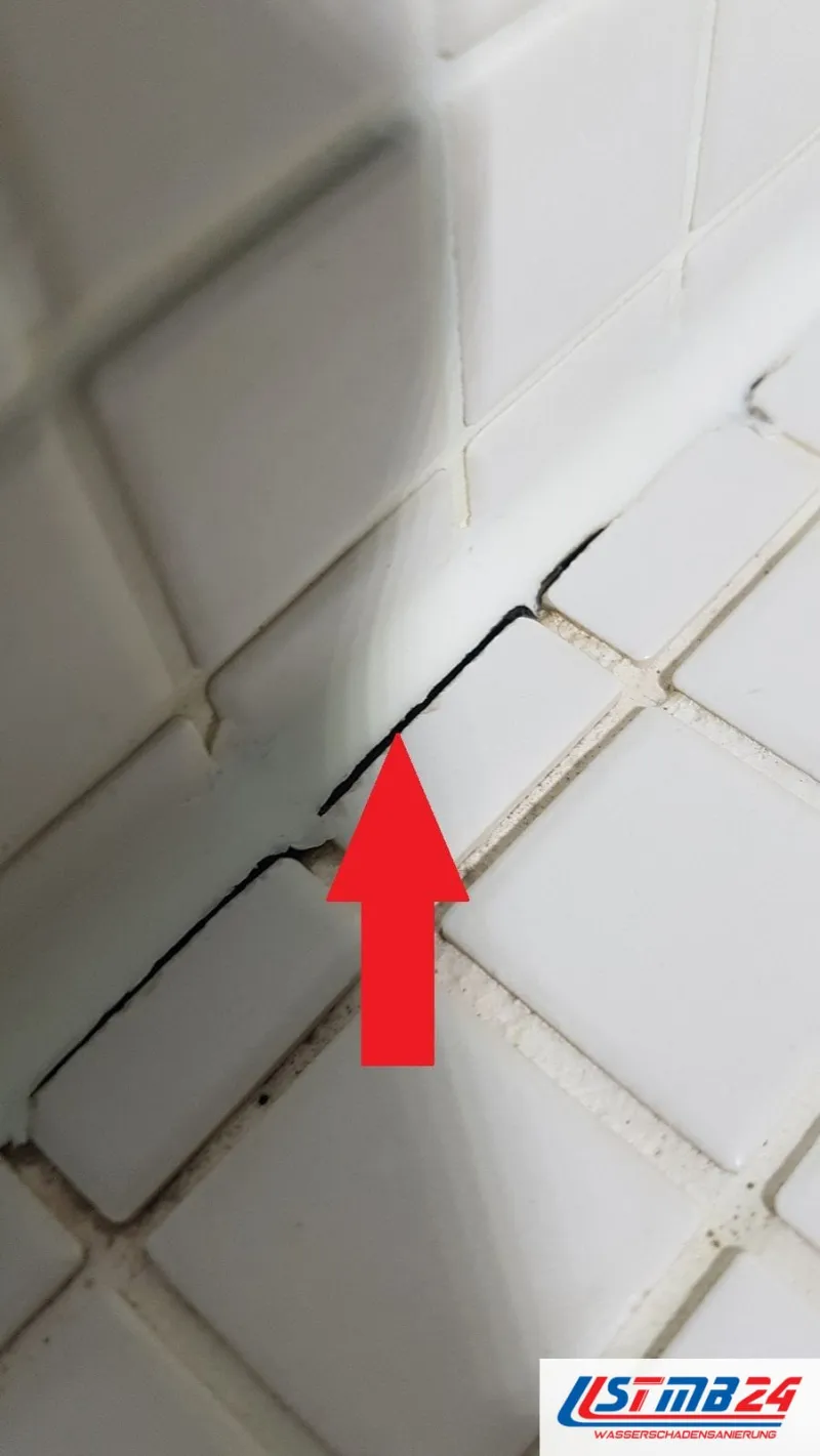 Fliesenarbeiten in der Dusche: offene Anschlussfuge zwischen Wand- und Bodenfliese, ein roter Pfeil zeigt auf den Spalt