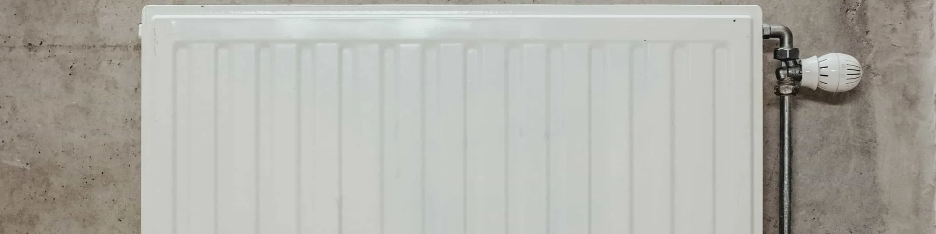 Heizung und Sanitärinstallation: weißer Plattenheizkörper mit Thermostatventil an einer Betonwand