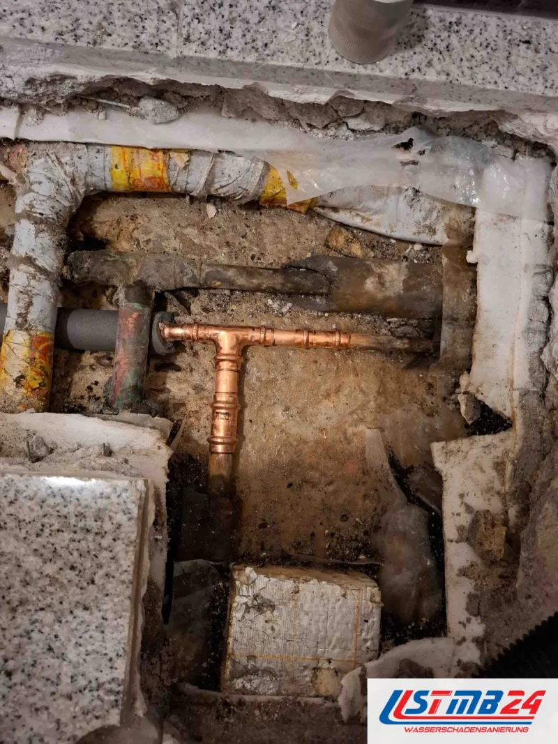 Heizung und Sanitärinstallation: neues Kupfer-T-Stück mit Pressfittings im geöffneten Steinboden zwischen alten Leitungen