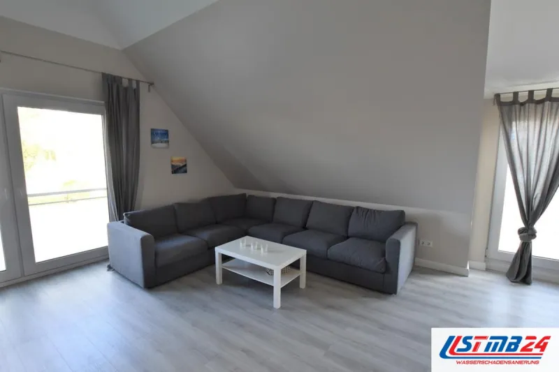 Fertig renoviert: Wohnzimmer unter der Dachschräge mit grauem Ecksofa, weißem Couchtisch und Laminat in heller Eichenoptik
