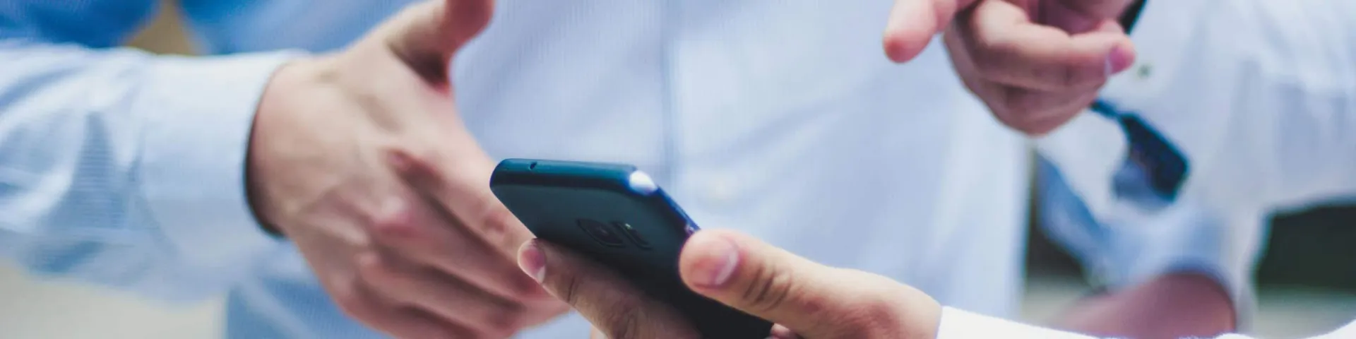 Kontakt: zwei Personen in hellblauen Hemden, eine hält ein Smartphone, die andere zeigt darauf