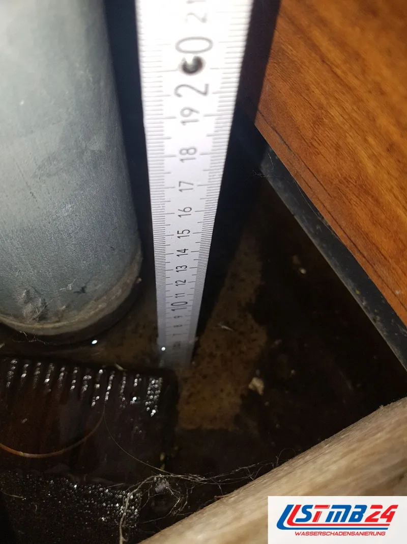 Kosten und Abwicklung: Zollstock im Hohlraum neben einem grauen Rohr, unten steht dunkles Wasser