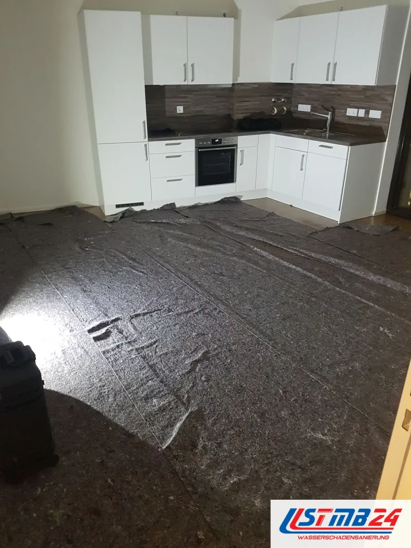 Küchenmontage: neue weiße Küche mit Hochschränken, Einbaubackofen und Rückwand in dunkler Holzoptik, Boden mit Vlies abgedeckt