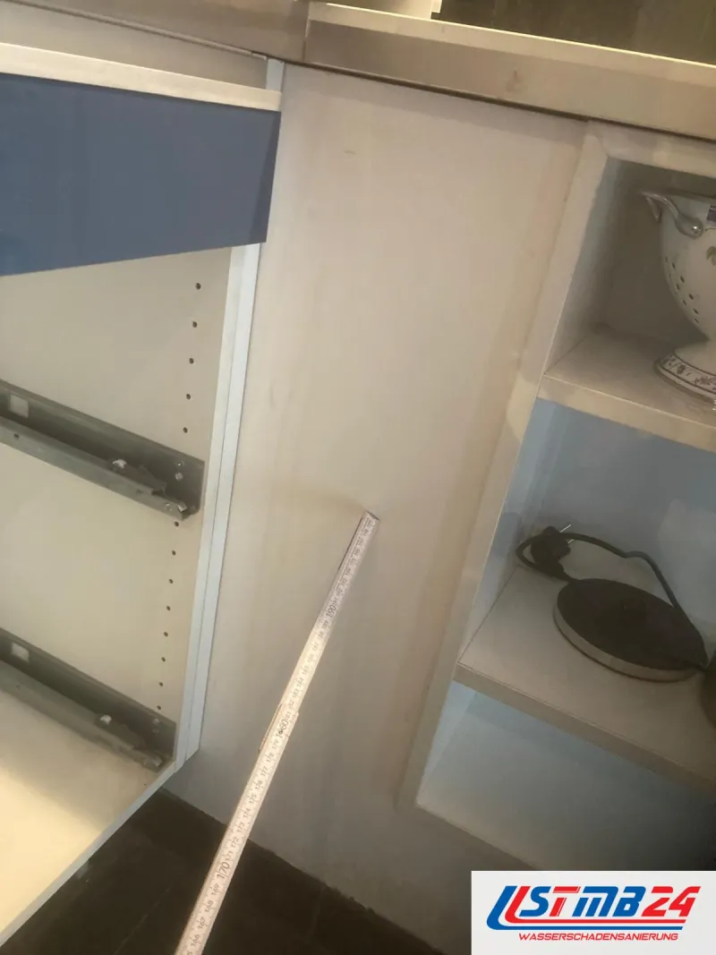 Küchenmontage: leerer Korpus mit Vollauszugsschienen, ein Zollstock liegt darin, rechts ein offenes Regal