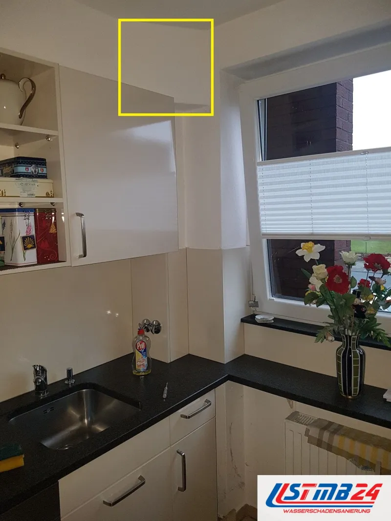 Küchenmontage: Küche mit weißen Fronten und schwarzer Arbeitsplatte, Spüle unter dem Fenster, ein gelber Rahmen markiert die Wand