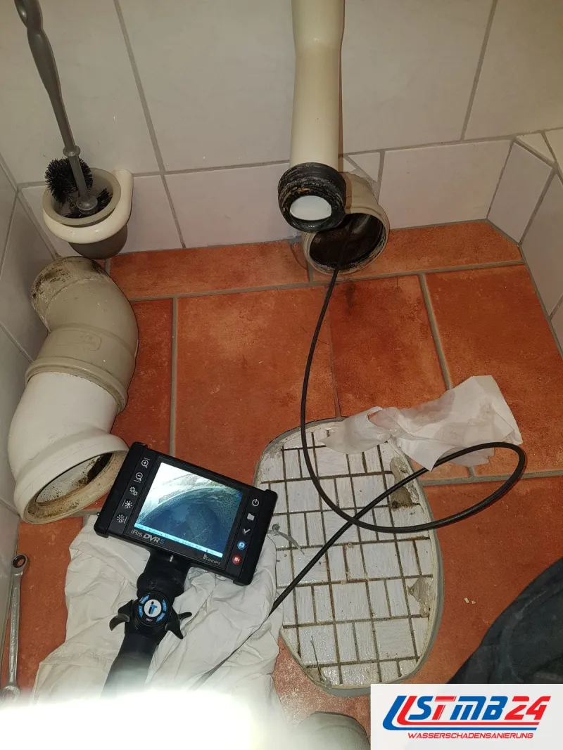 Leckageortung im Abfluss: WC abgebaut, Videoendoskop im Anschluss, der Monitor zeigt das Rohrinnere, daneben der ausgebaute Bogen