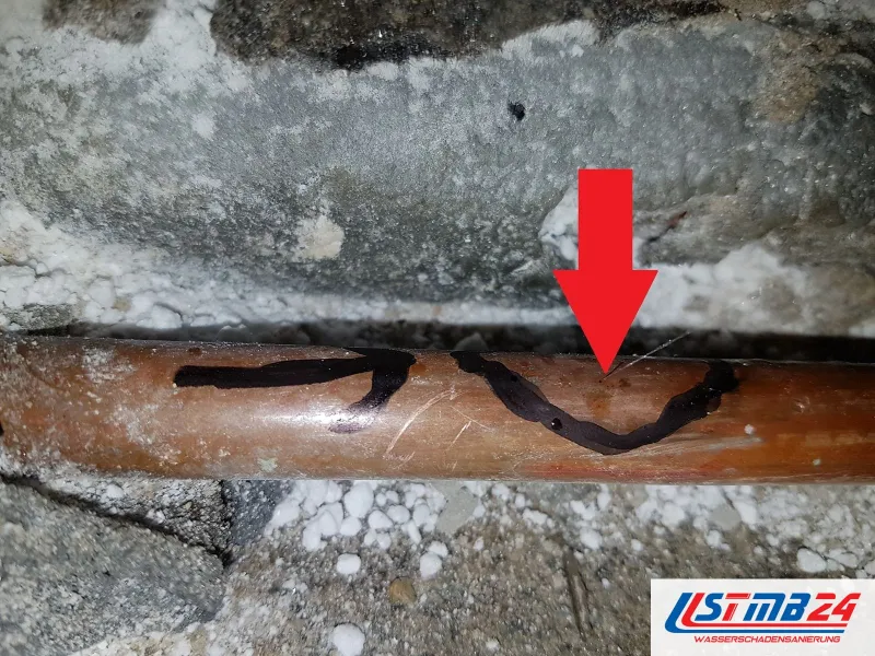 Leckageortung abgeschlossen: Kupferrohr im geöffneten Estrich, ein roter Pfeil zeigt auf die undichte Stelle, darunter Dämmkügelchen