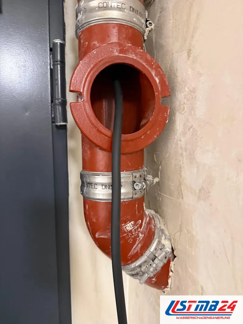 Leckageortung im Fallrohr: Kabel der Rohrkamera in der offenen Reinigungsöffnung eines roten Gussrohrs mit Edelstahlverbindern