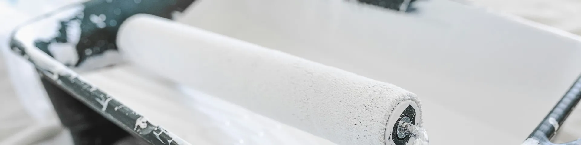 Maler- und Lackierarbeiten: Farbrolle mit weißer Wandfarbe in einer Farbwanne