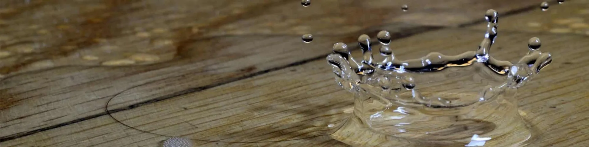 Schadenwissen zum Wasserschaden: Wassertropfen schlägt auf einen nassen Holzboden und bildet eine Wasserkrone
