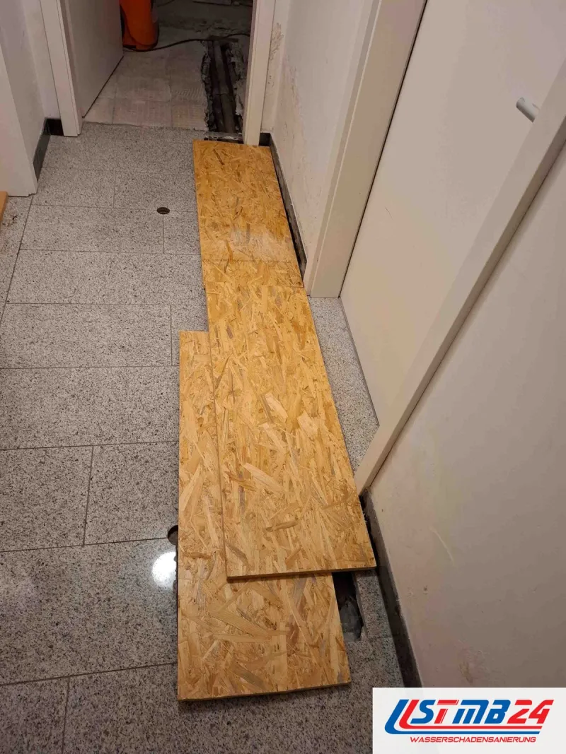 Wasserschaden in Geesthacht: Flur mit Granitboden, OSB-Platten liegen als Laufweg, hinten ist der Boden für die Leitungen geöffnet