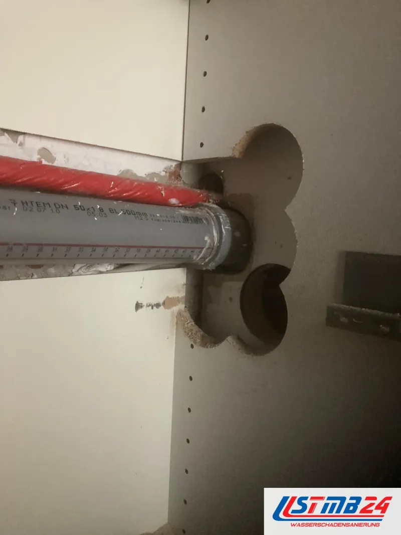 Küchenmontage in Geesthacht: Korpusrückwand mit ausgesägter Durchführung, ein graues HT-Rohr und ein rot gedämmtes Rohr laufen hindurch